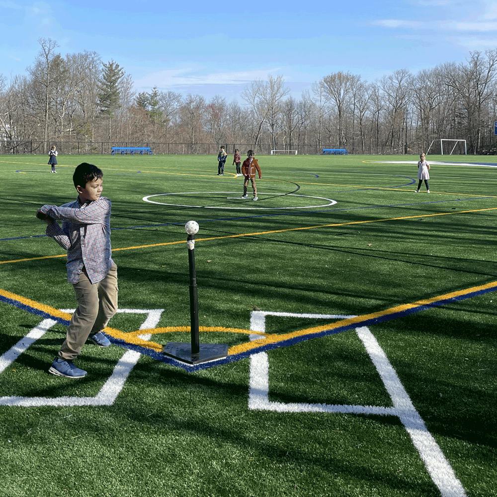 Child swinging a bat at a tee ball stand on a field