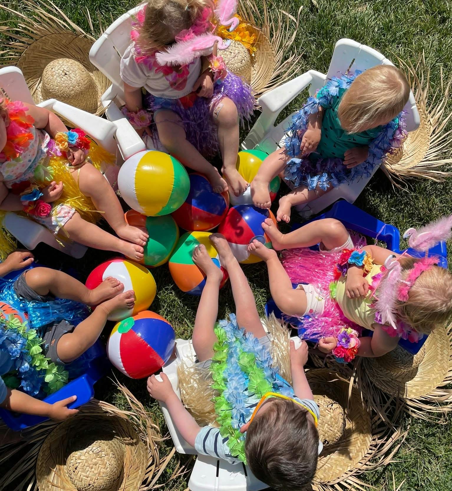 Several children in colorful leis and grass skirts sitting with beach balls