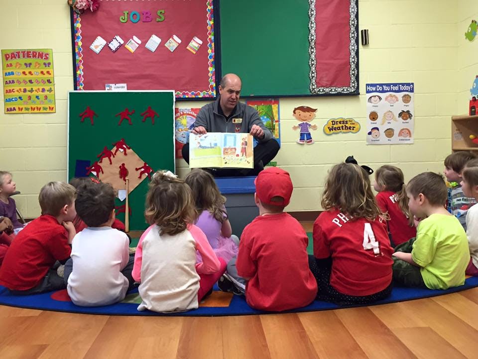 Adult reading a book to a group of children sitting on a rug