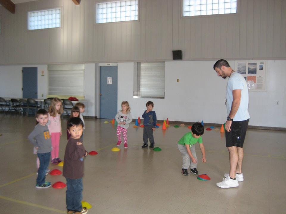 Adult supervising children playing with colorful cones indoors