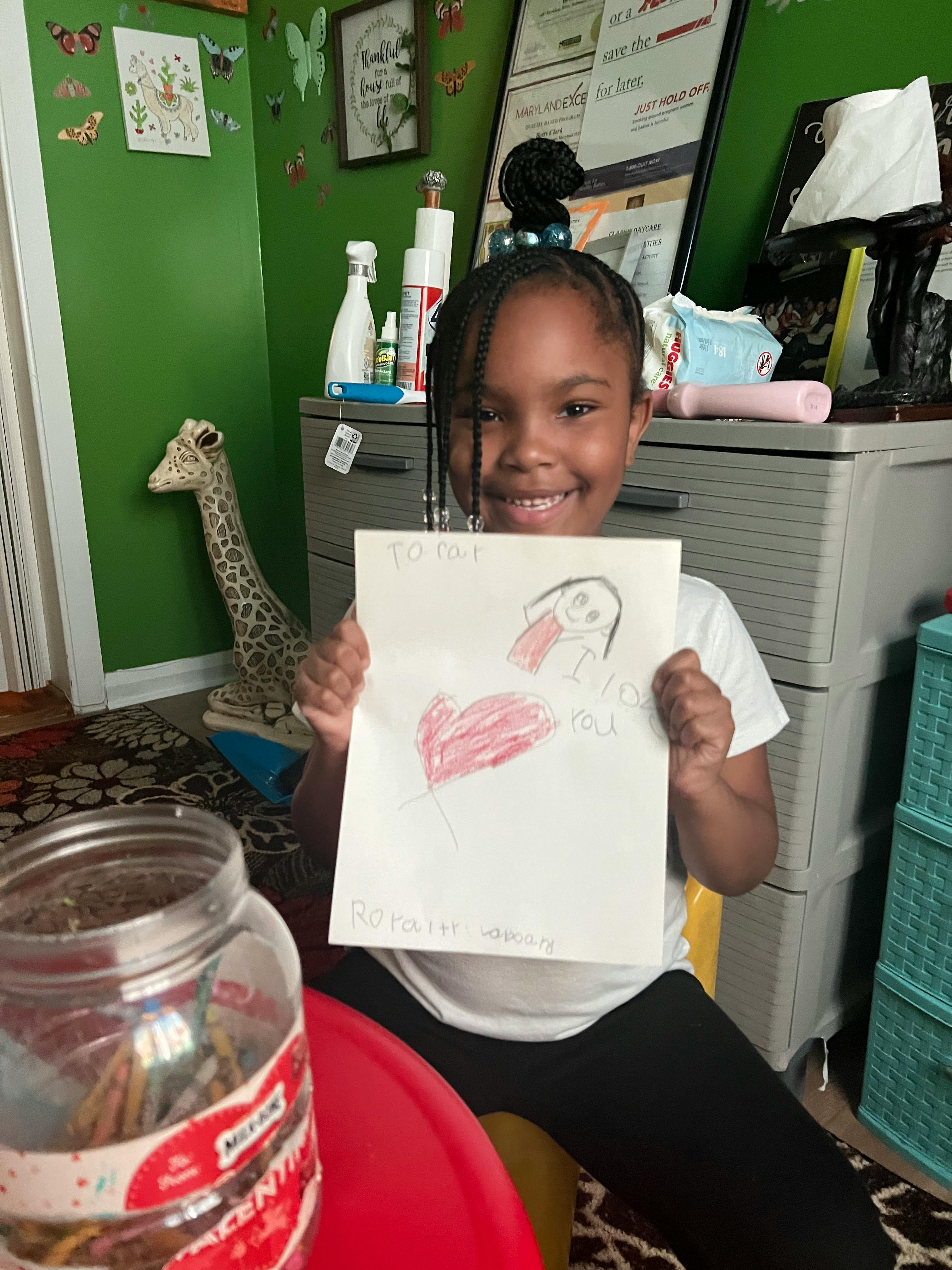 Child holding up a drawing of a heart and a bird