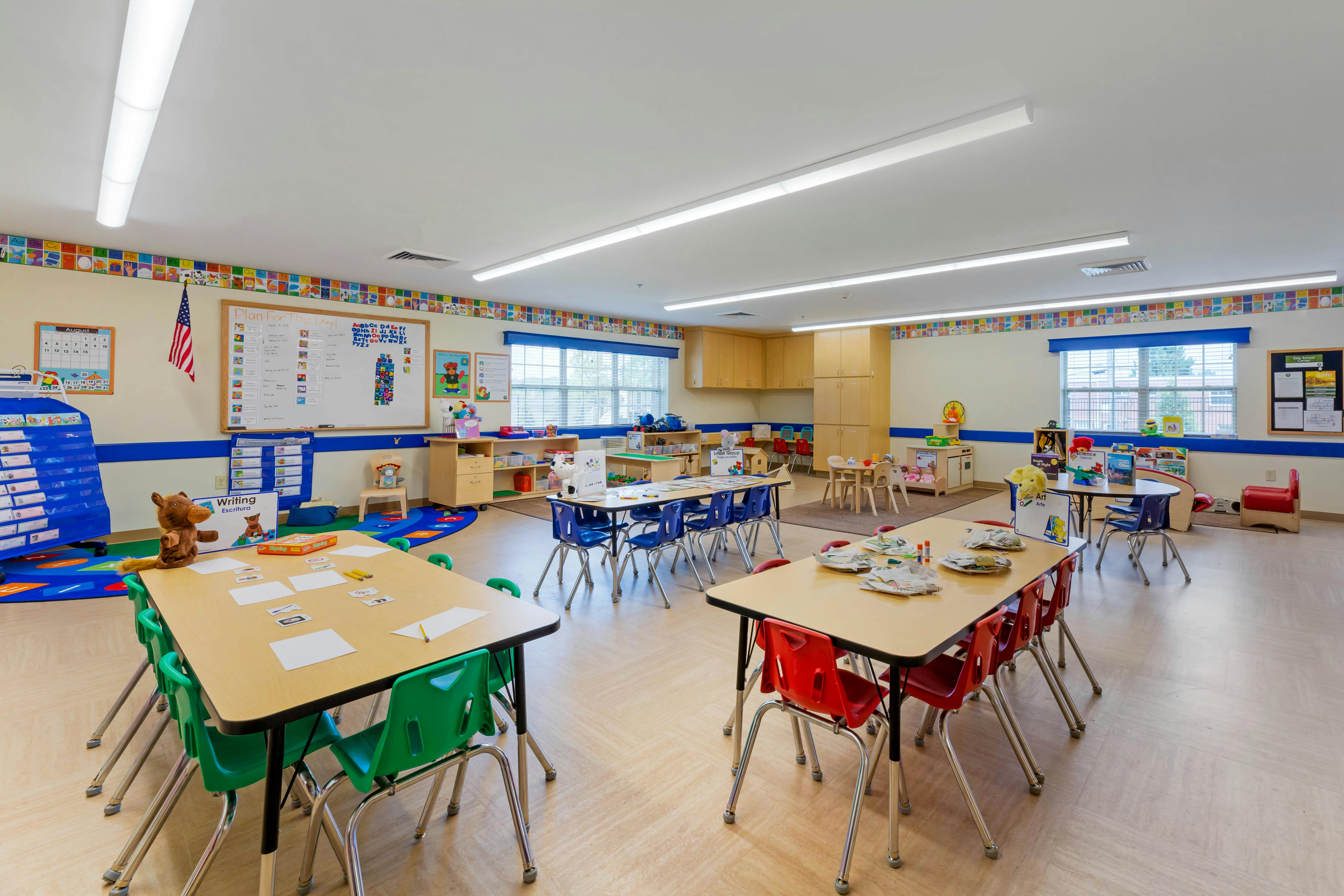 Empty classroom with multiple tables, chairs, and learning materials