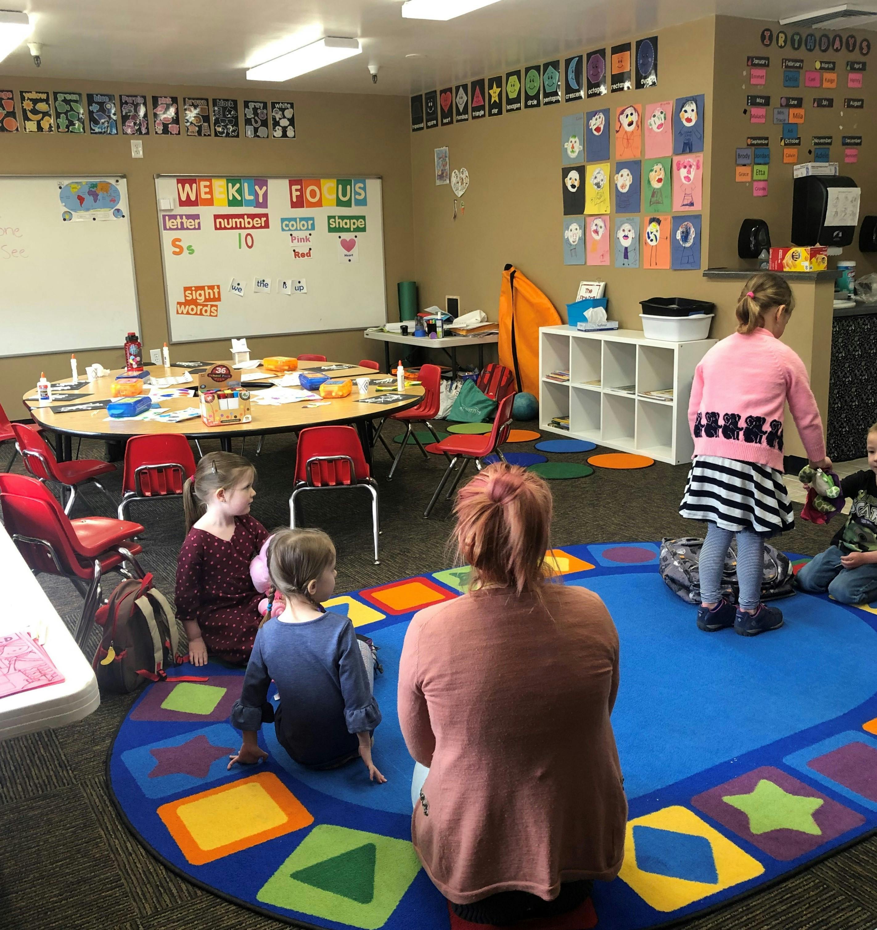 Adult and children sitting on a colorful rug in a classroom