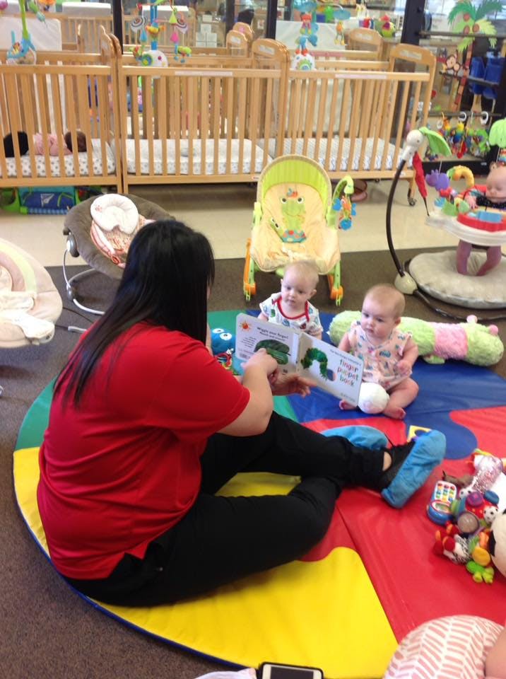 Person reading a book to two babies on a colorful mat