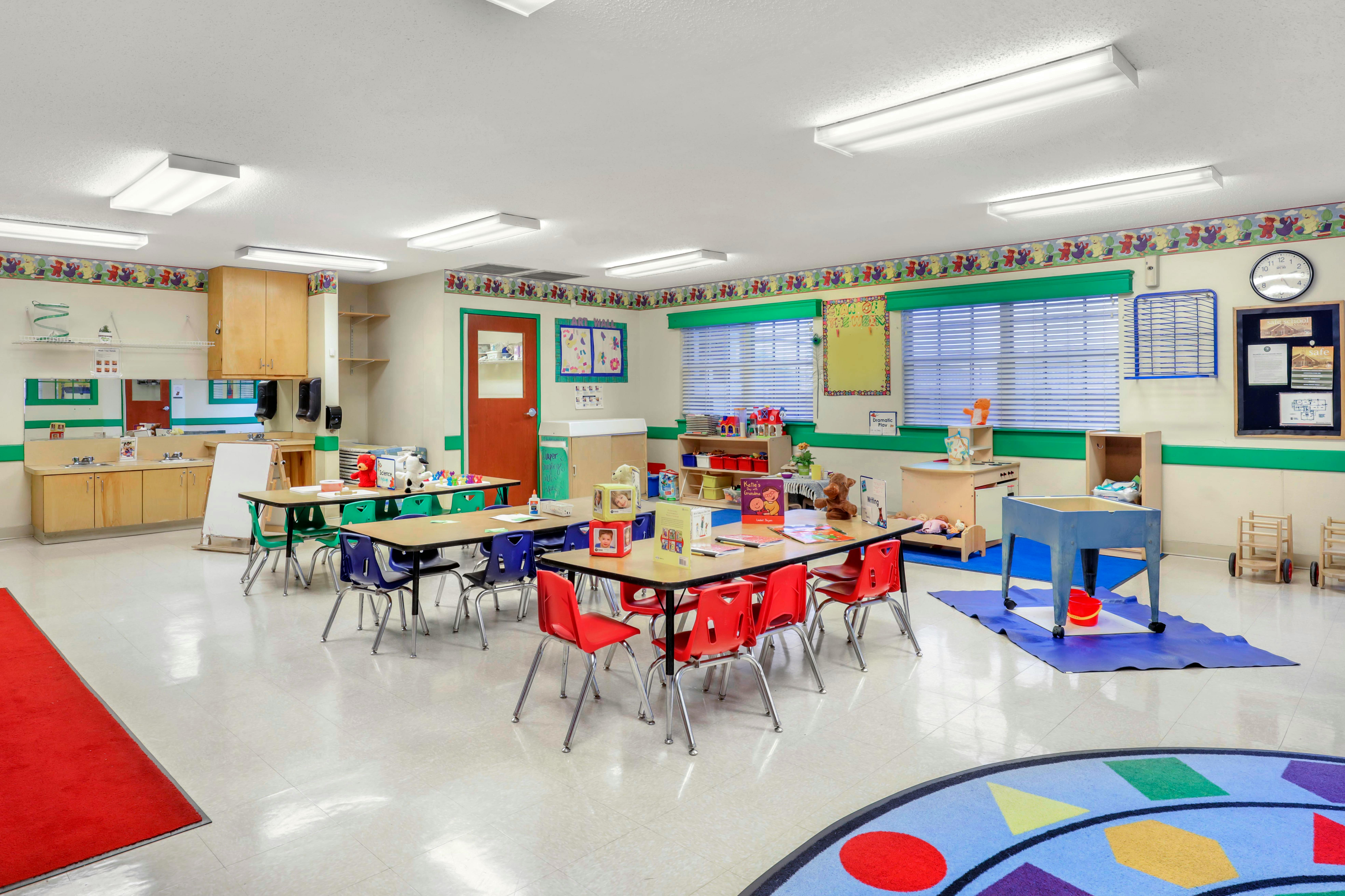 An empty early childhood classroom with multiple tables and chairs, play areas