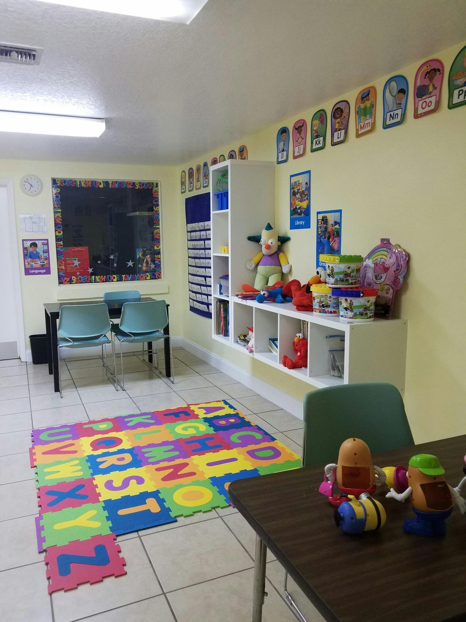 Classroom with alphabet mat, tables, chairs, and shelves with toys