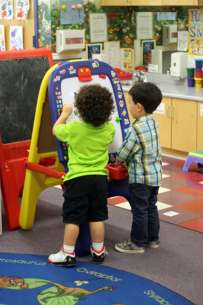 Two children drawing on an easel in a classroom
