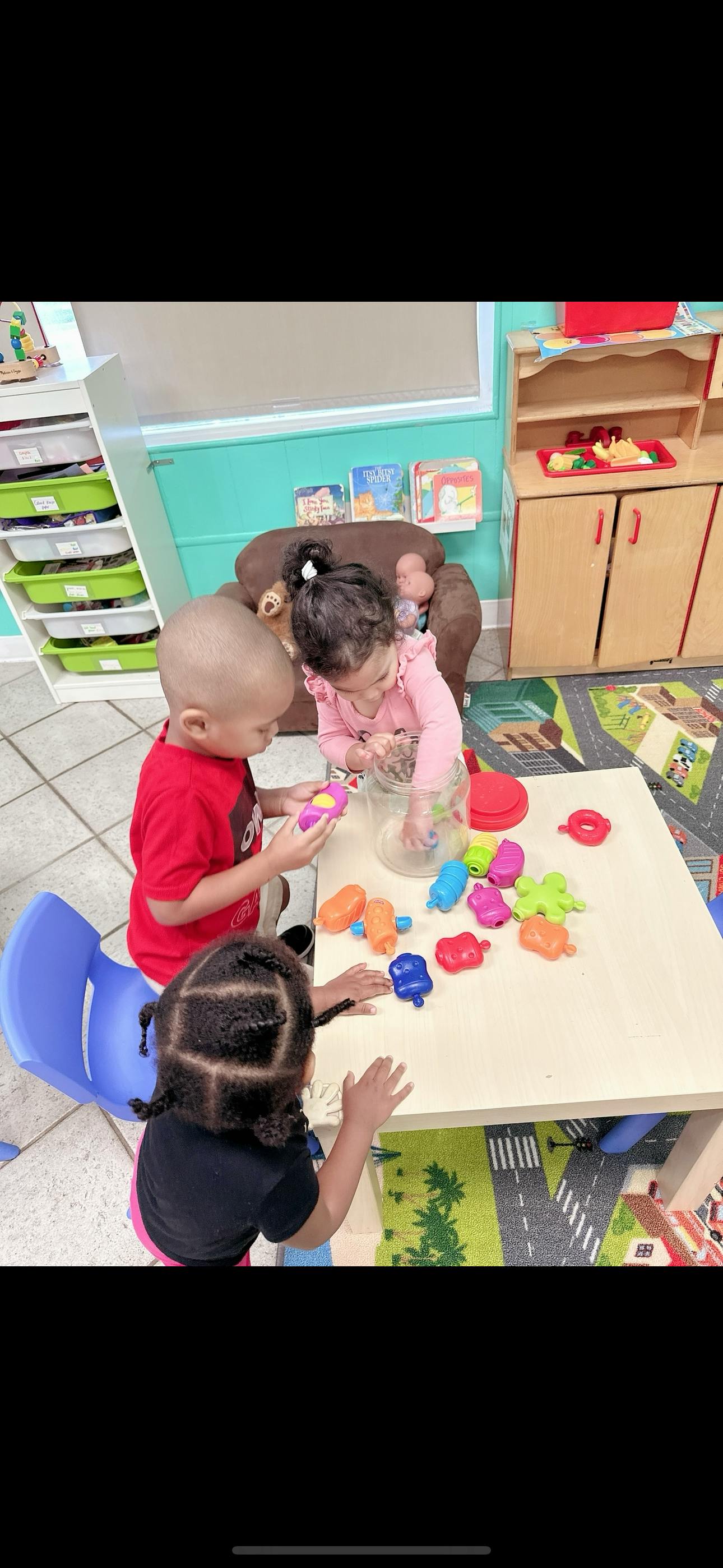 Three children playing with colorful toys at a small table in a classroom