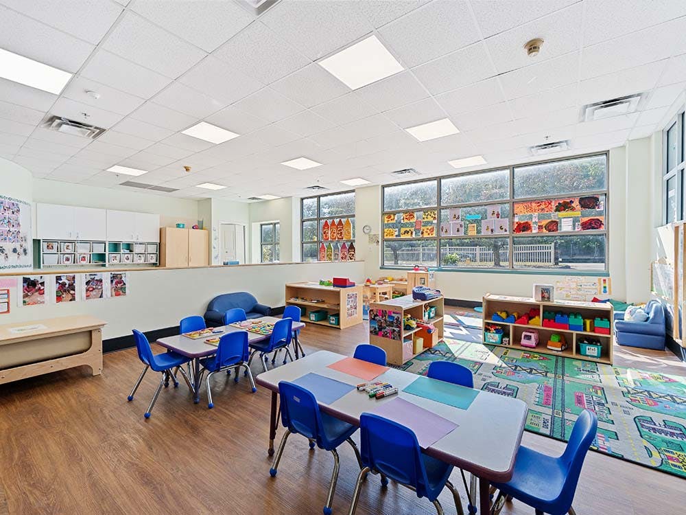 Empty colorful preschool classroom with small tables, chairs, and play areas