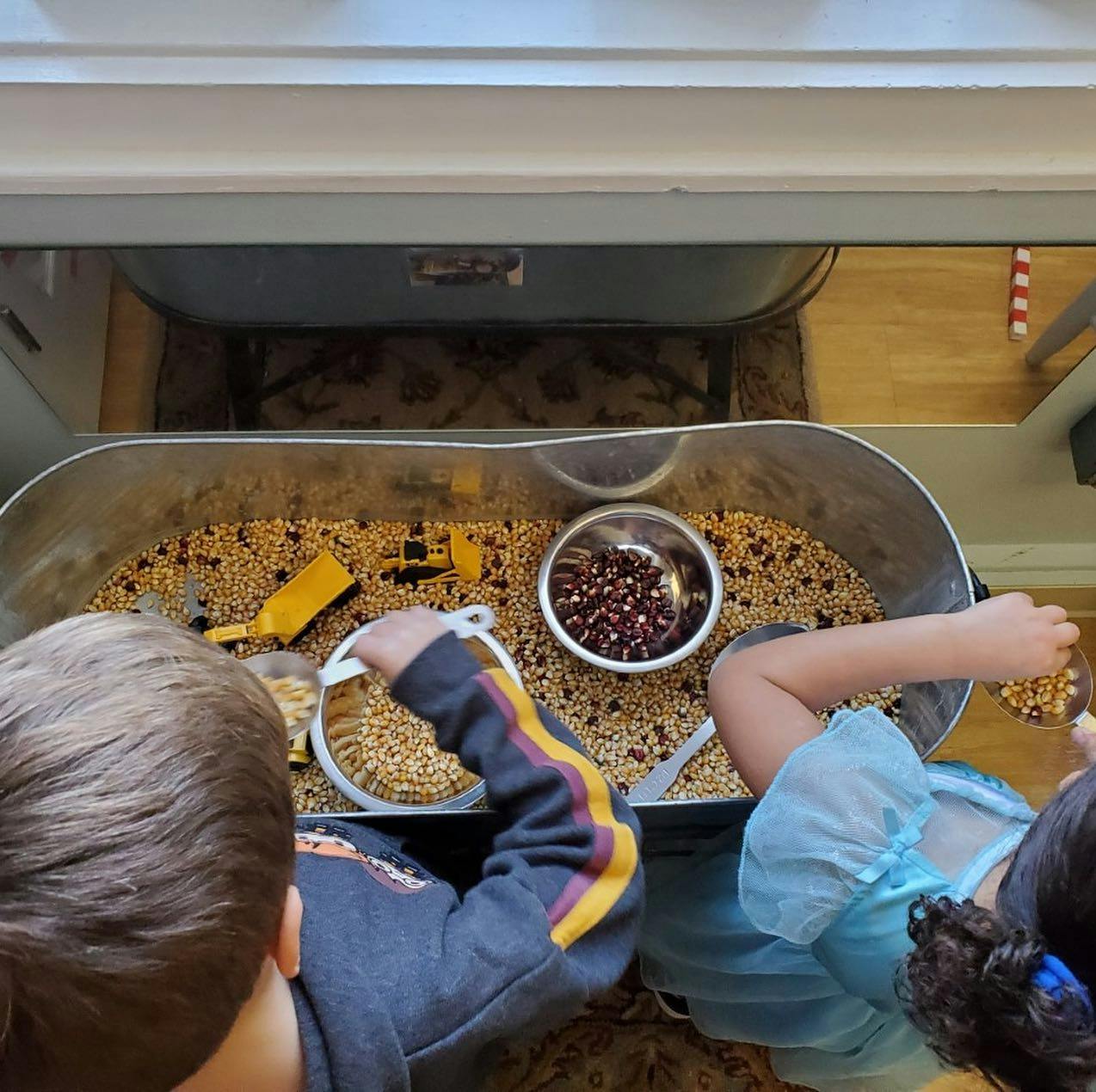 Two children playing with grains and beans in a sensory bin