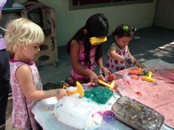 Three children playing with toys and colorful materials on a table