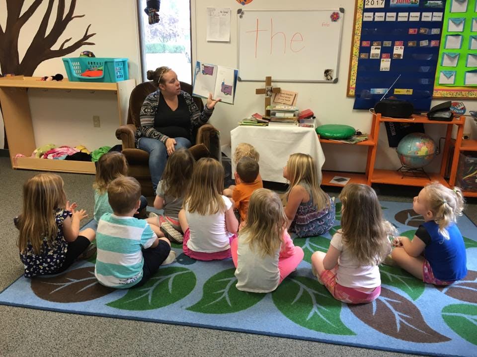 Adult reading a book to a group of children in a classroom