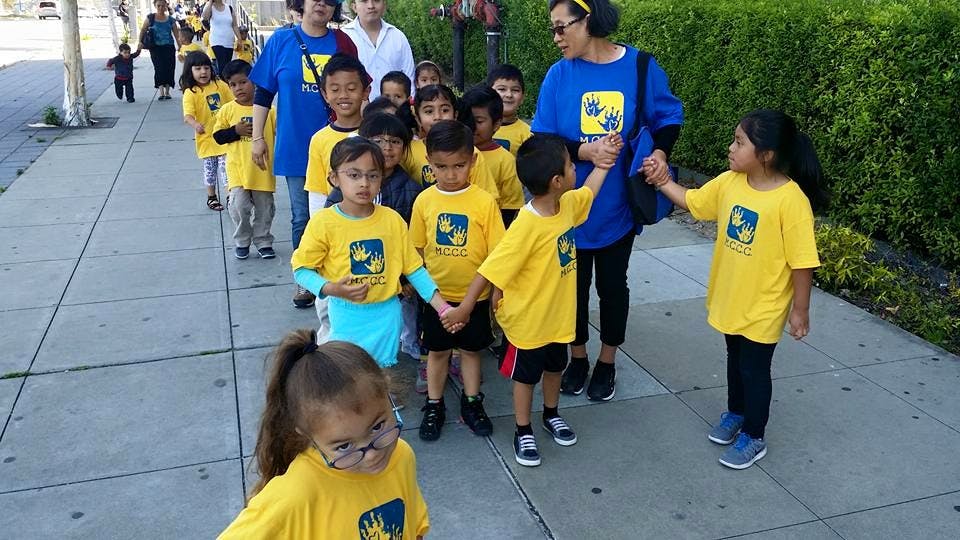 Adults and children in yellow shirts walking in a line on a sidewalk