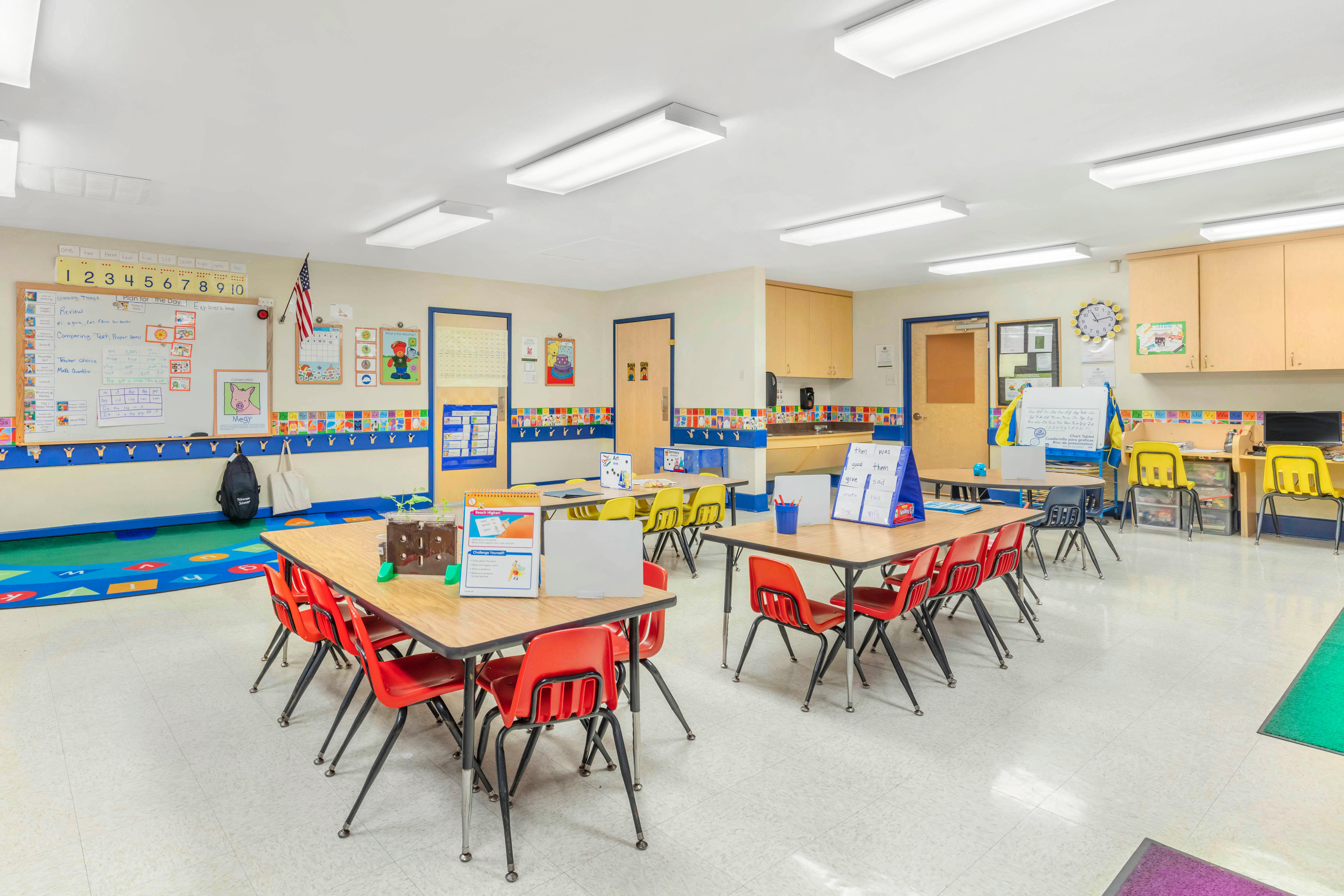 Empty classroom with small tables and chairs, whiteboards, and educational posters