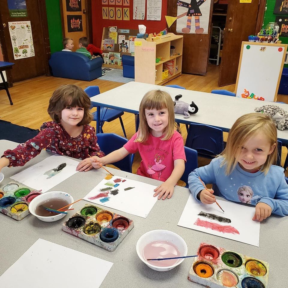 Three children painting at a table in a classroom