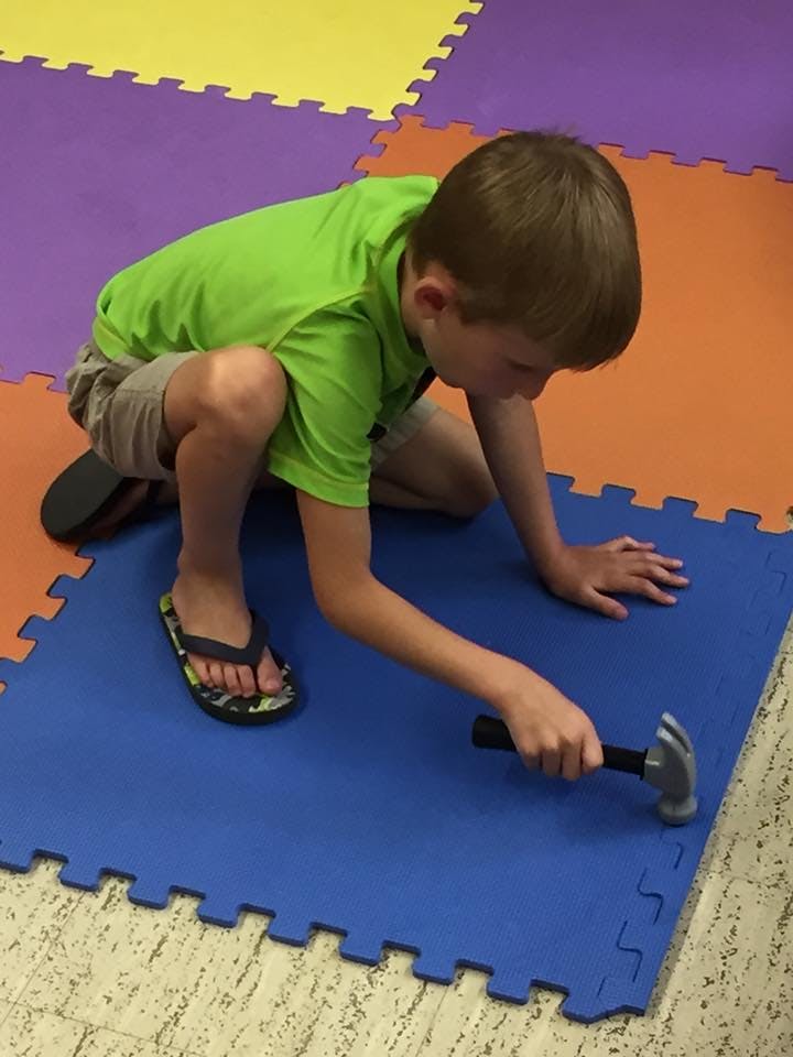 Child kneeling on floor holding a hammer