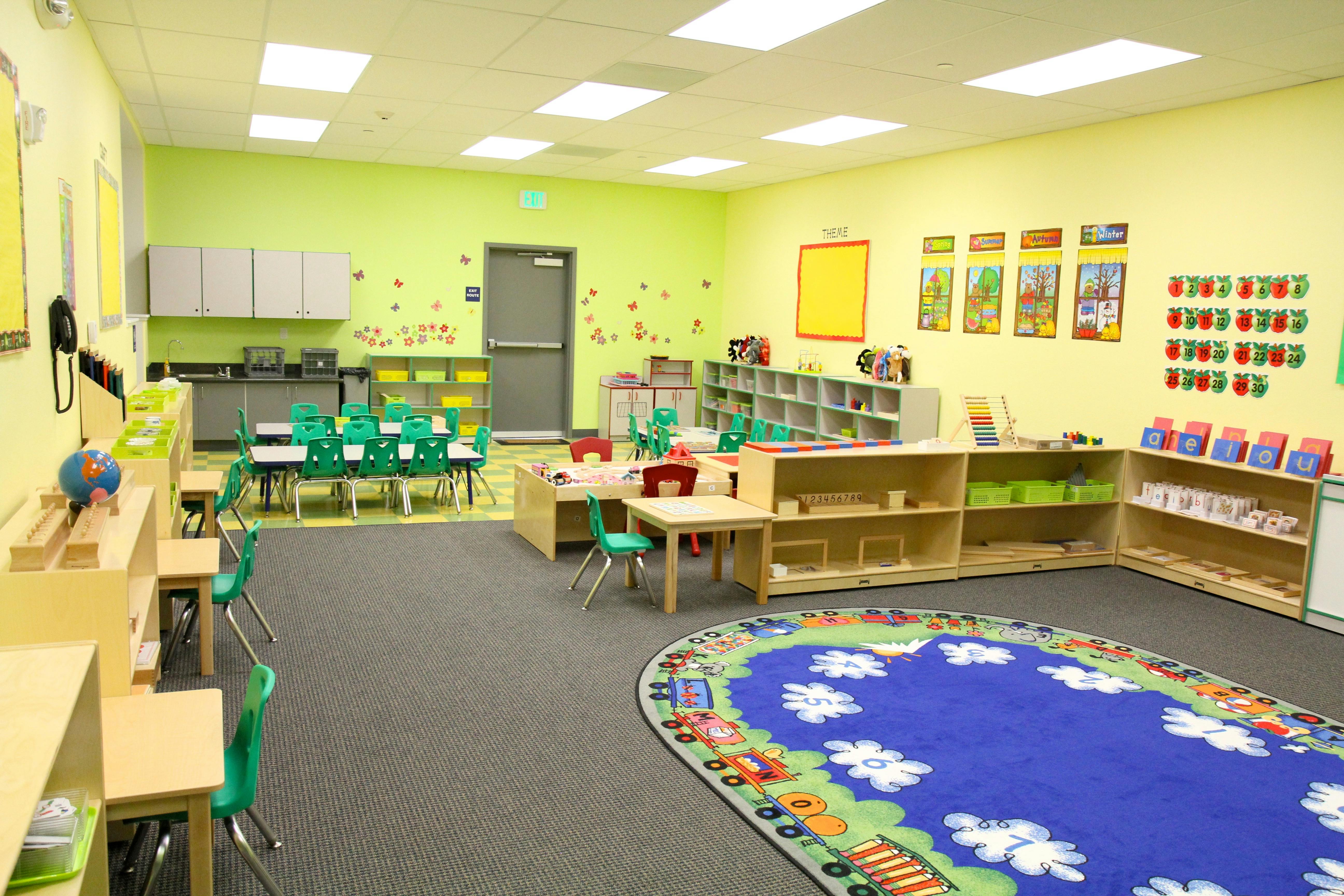Classroom with small tables and chairs, shelves, and a colorful rug