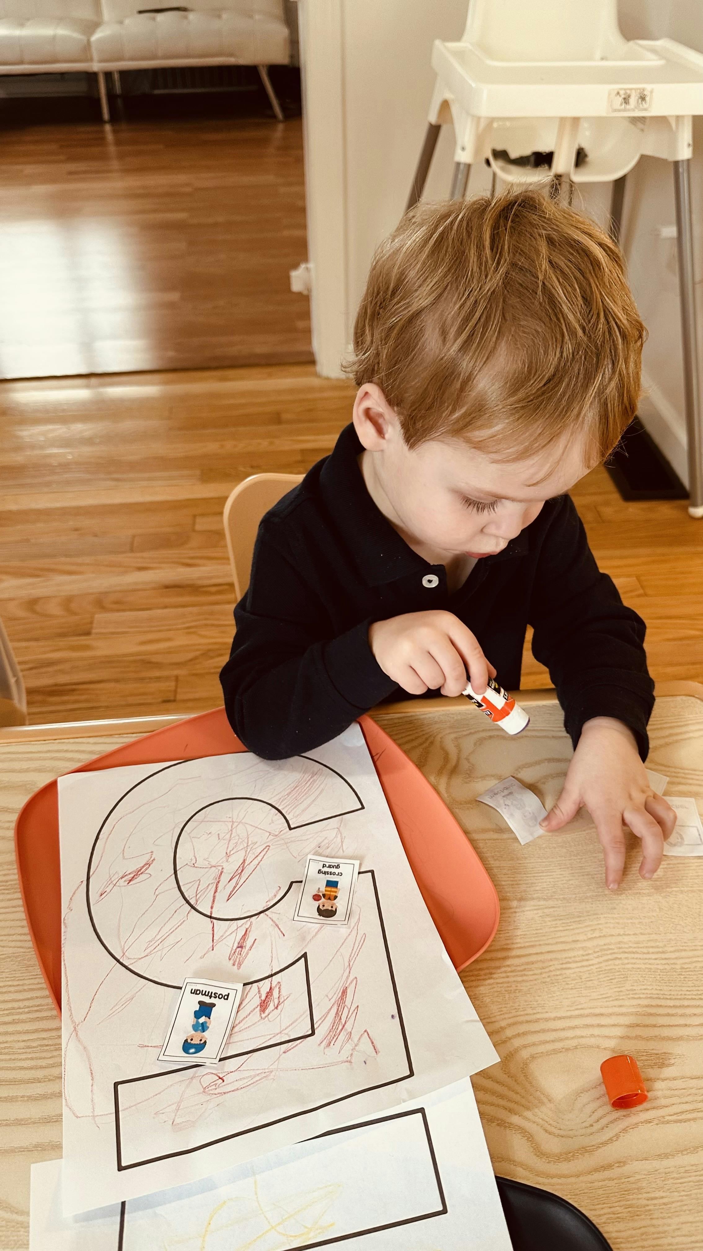 Child gluing paper onto a large letter C outline