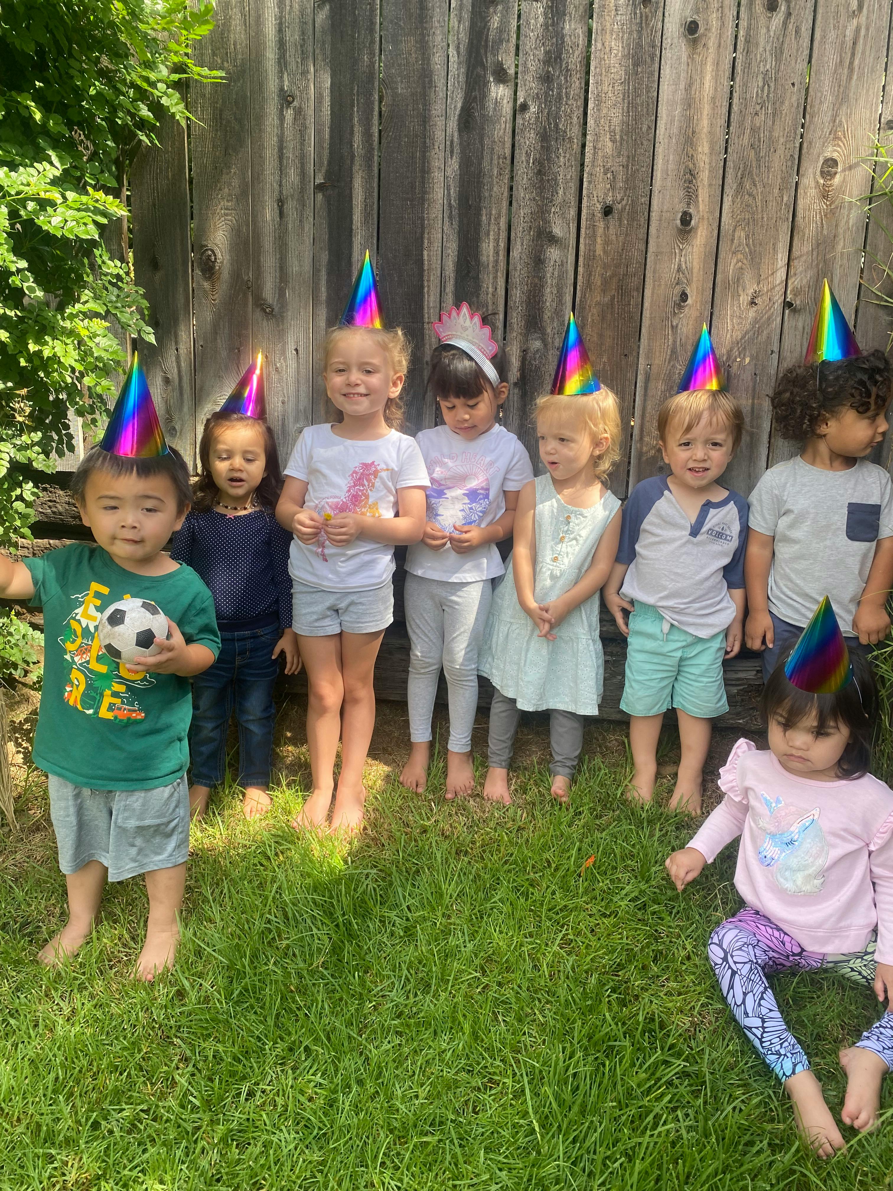 Group of children wearing party hats in a line against a wooden fence