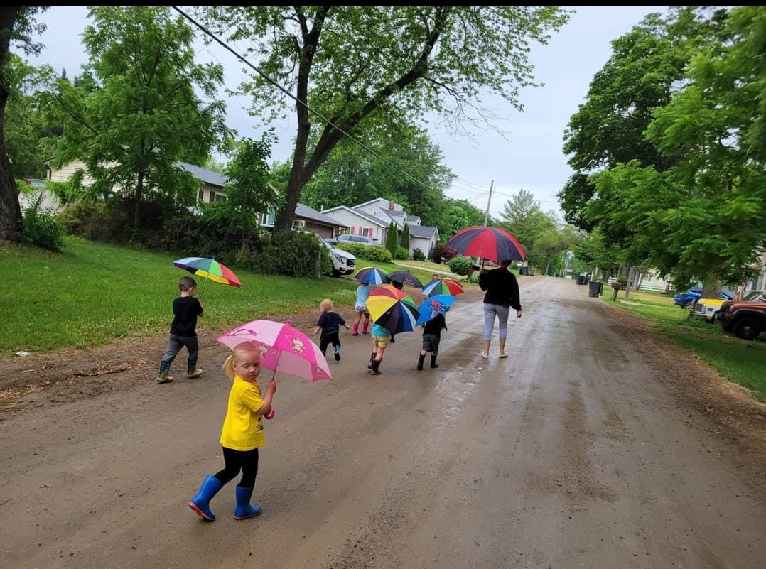 Children and an adult walking on a wet road with umbrellas
