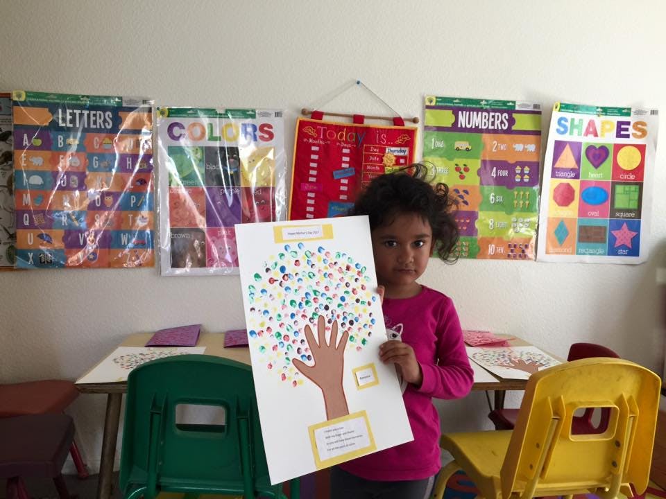 Child holding up a drawing of a tree with colorful dots for leaves