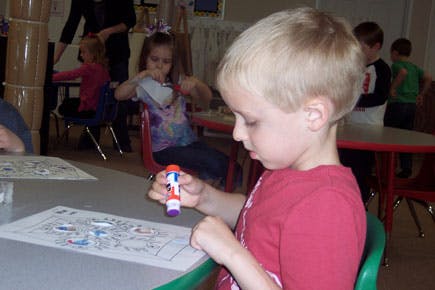 Child holding a glue stick over a drawing