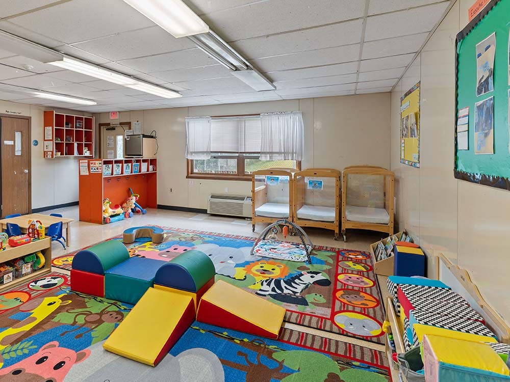 Childcare classroom with colorful rugs, soft play equipment, and three cribs