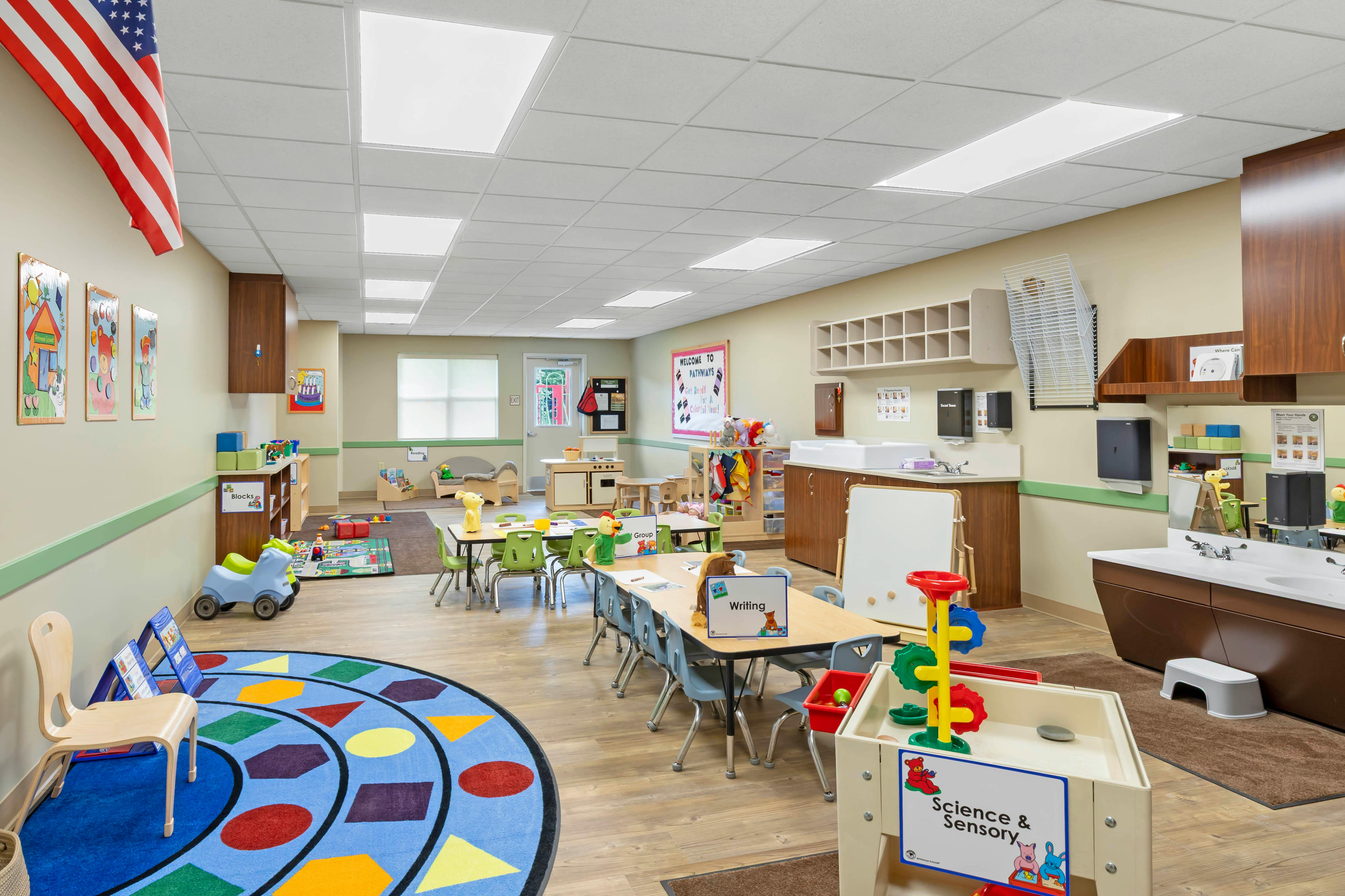 Classroom with child-sized tables and chairs, a sink area, and various play equipment