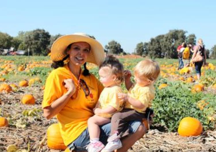 Person in a hat holding two children in a pumpkin patch