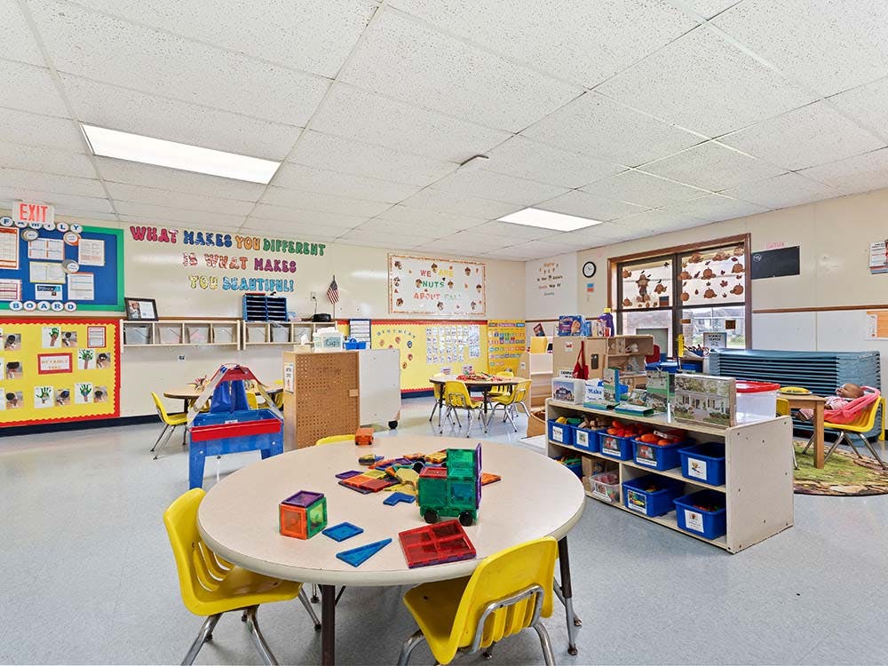 Classroom with tables, chairs, toys, and bulletin boards, with one child sleeping