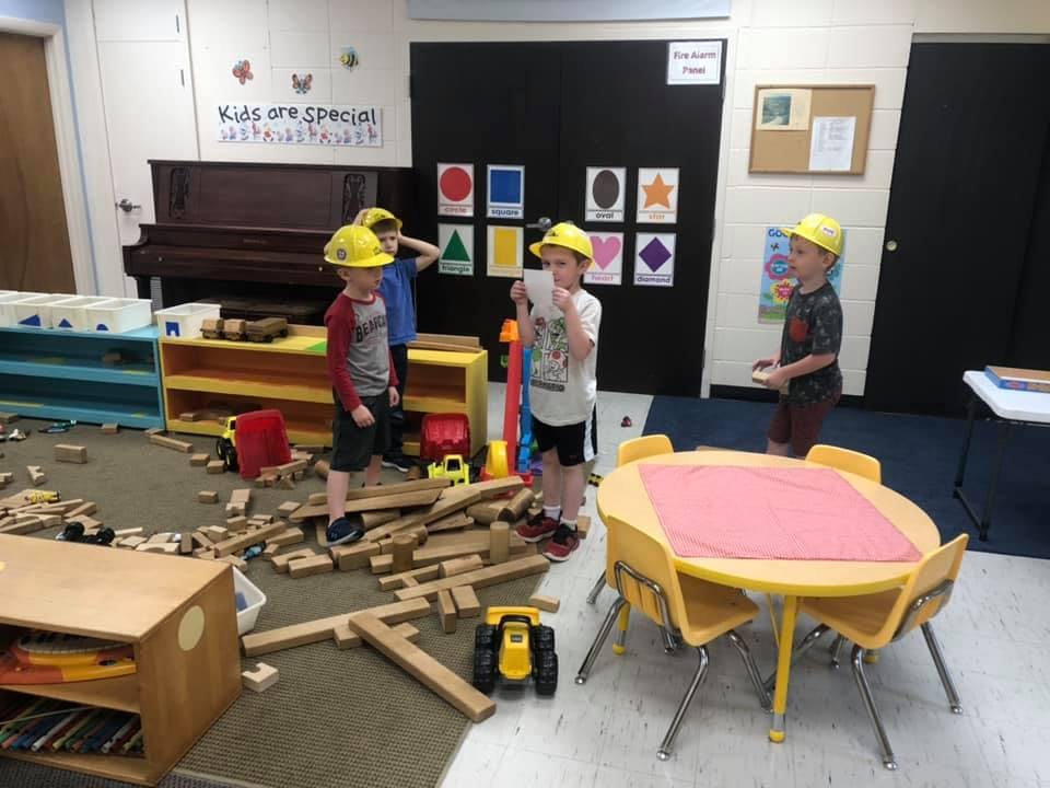 Children in hard hats playing with wooden blocks in a classroom