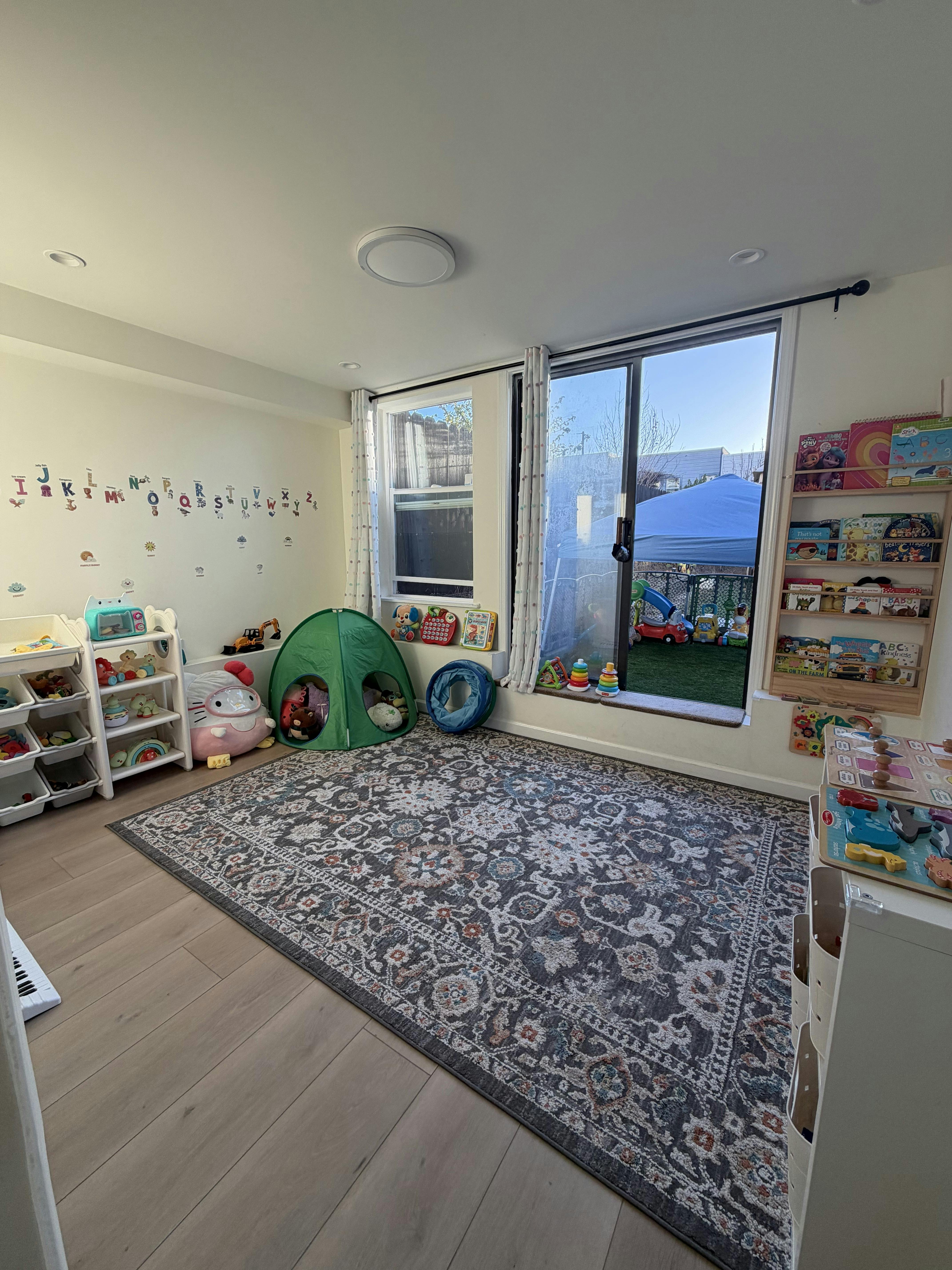 Playroom with toys, a play tent, shelves, and a rug