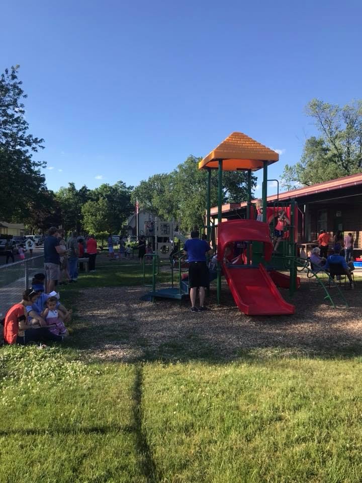 People and children on a playground with a slide and play structure