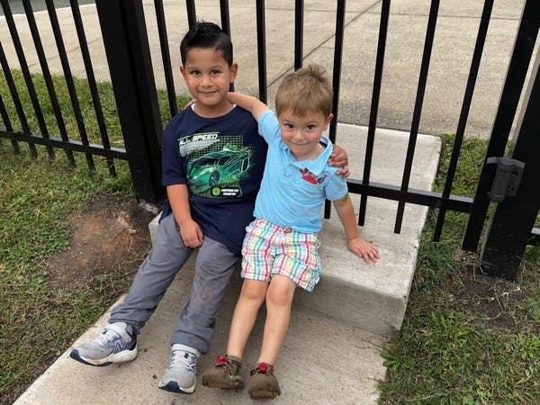 Two children sitting on a concrete step next to a black fence