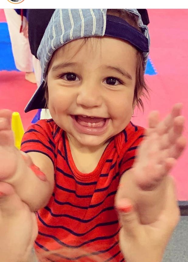 Child in a striped shirt and baseball cap with hands raised