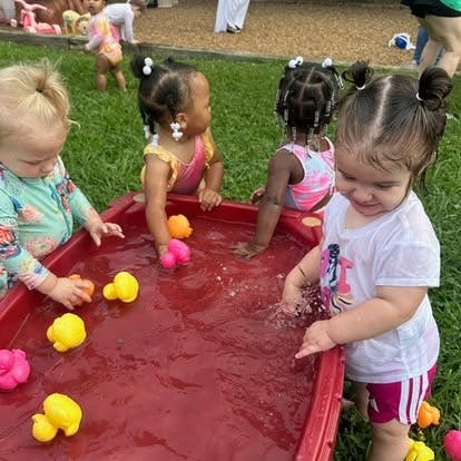 Four children playing with water and toys in a red bin