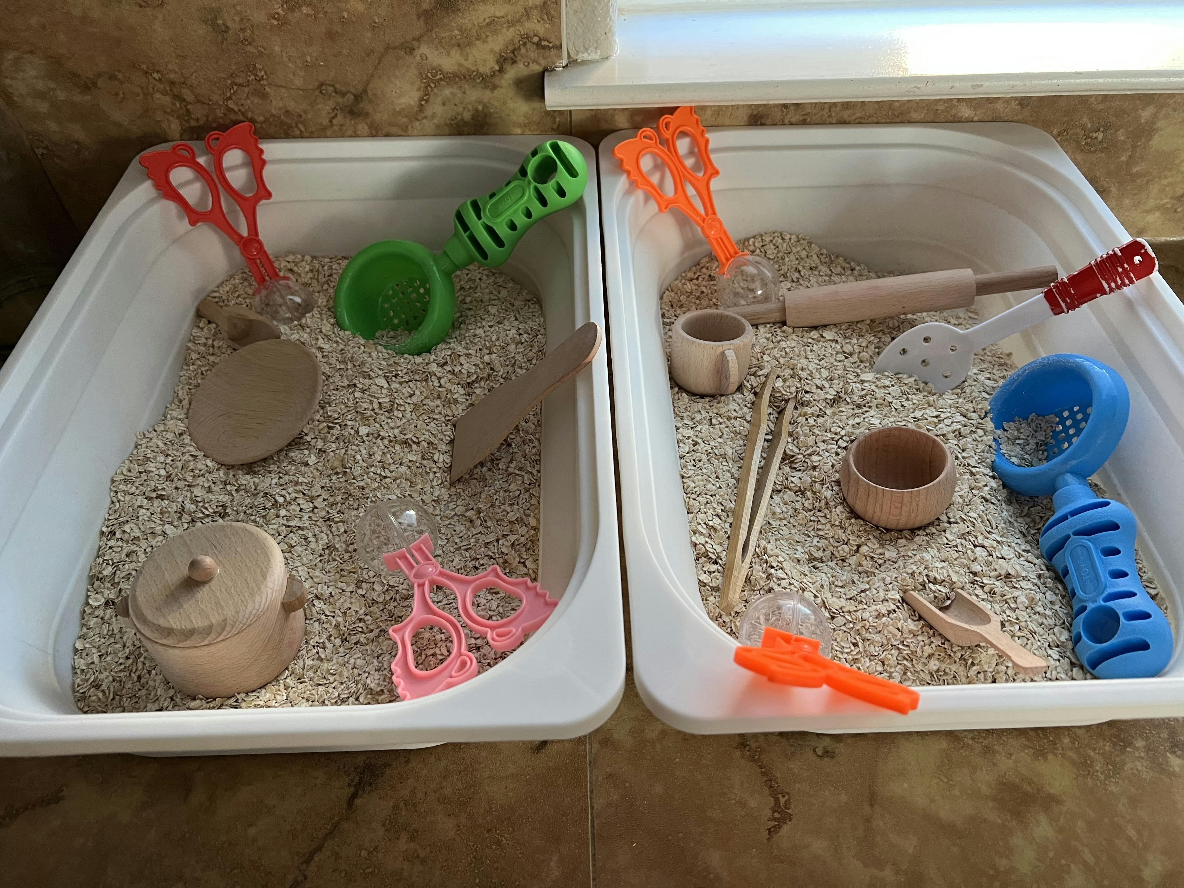 Two white bins with oatmeal and various sensory play tools