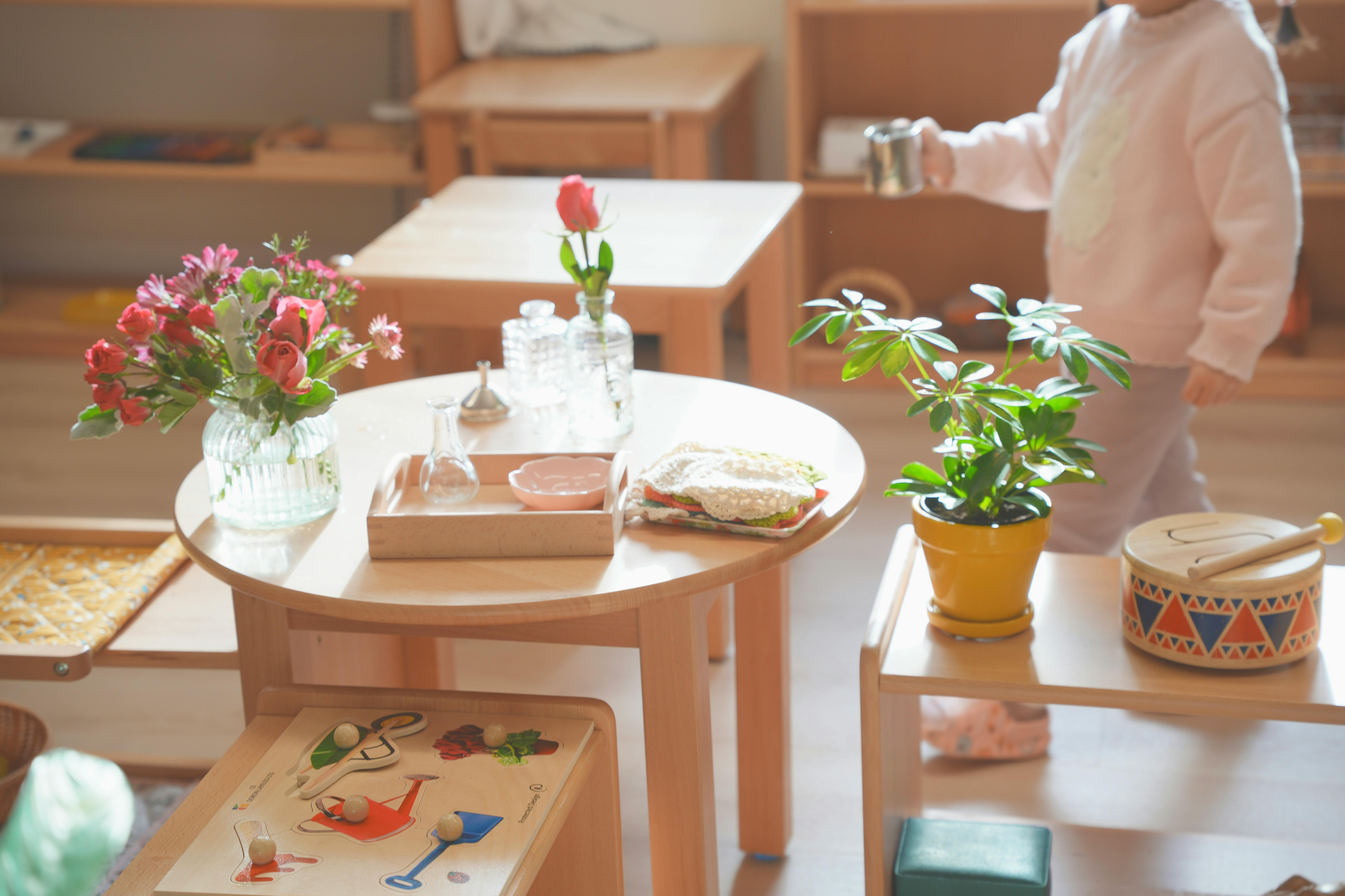 Child walking past a table with flowers and a plant in a classroom