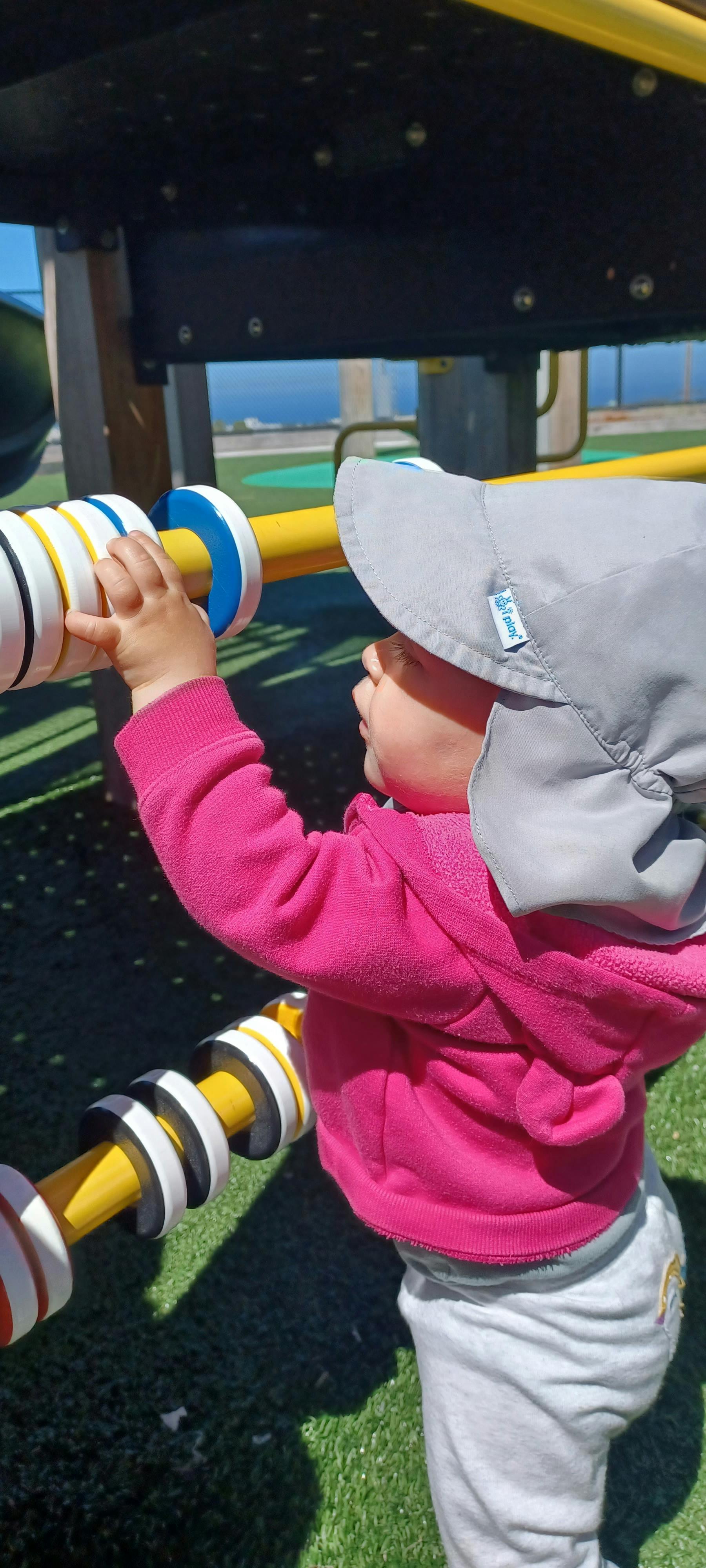 Child in a sun hat playing with a colorful toy on a playground