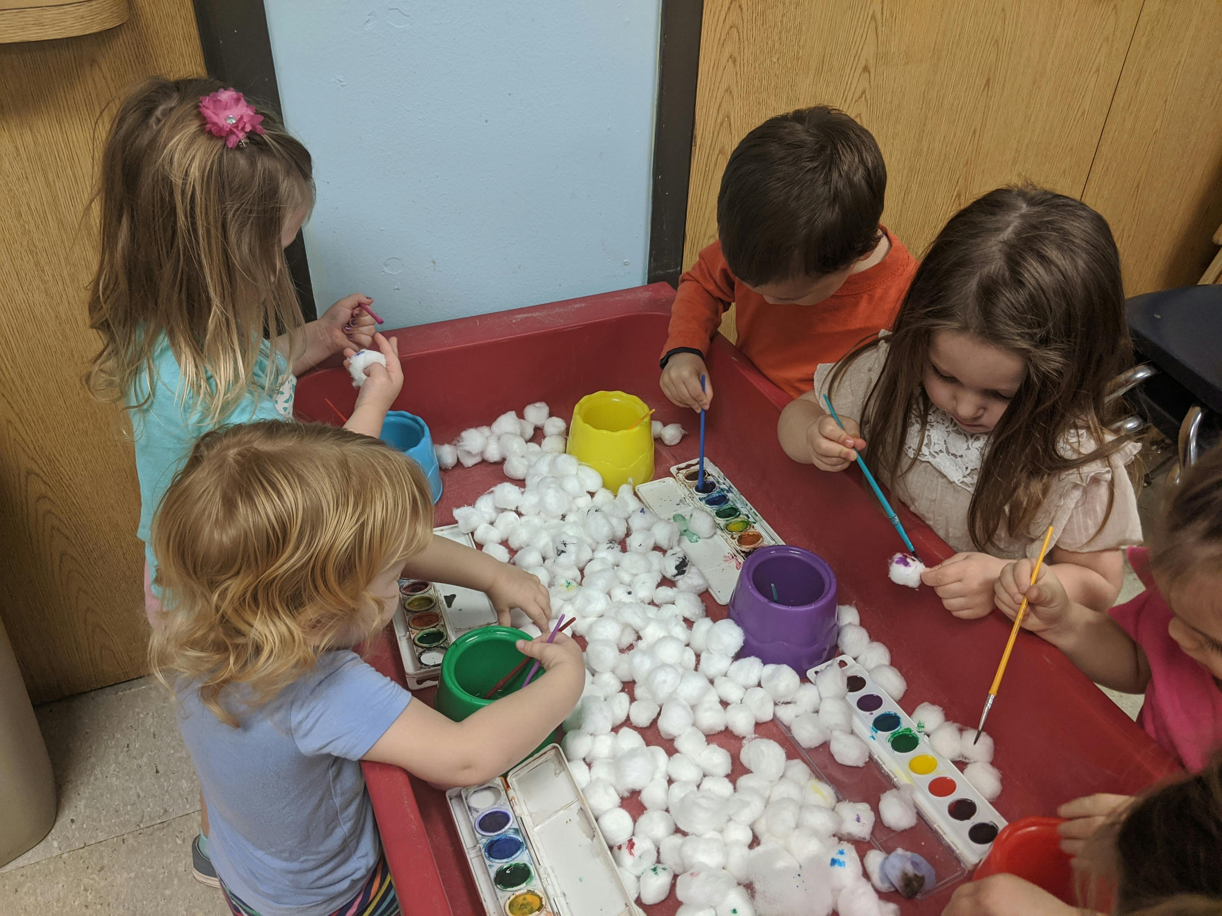 Children painting cotton balls at a table