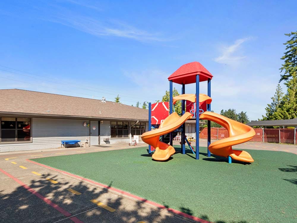 Playground with orange slides and red and blue climbing structure next to a building