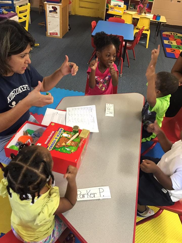 Adult and children at a table with a game, some giving thumbs up