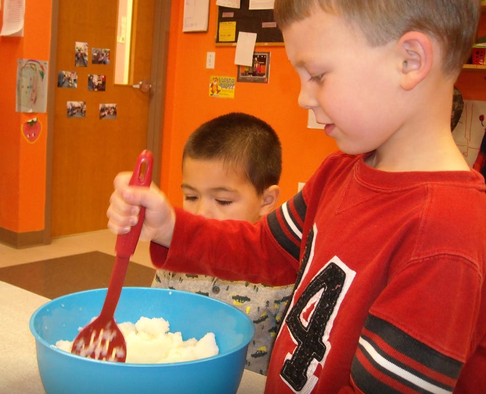 Child stirring white contents in a blue bowl with a red spoon