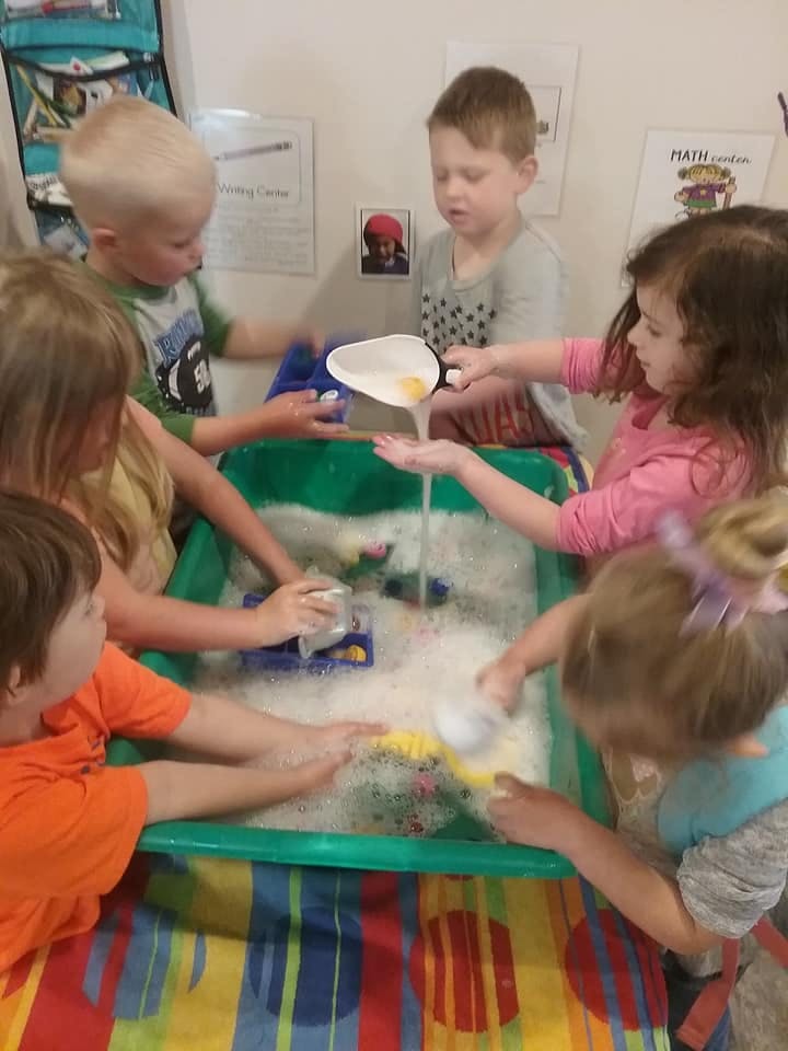 Children playing with water and bubbles in a green bin