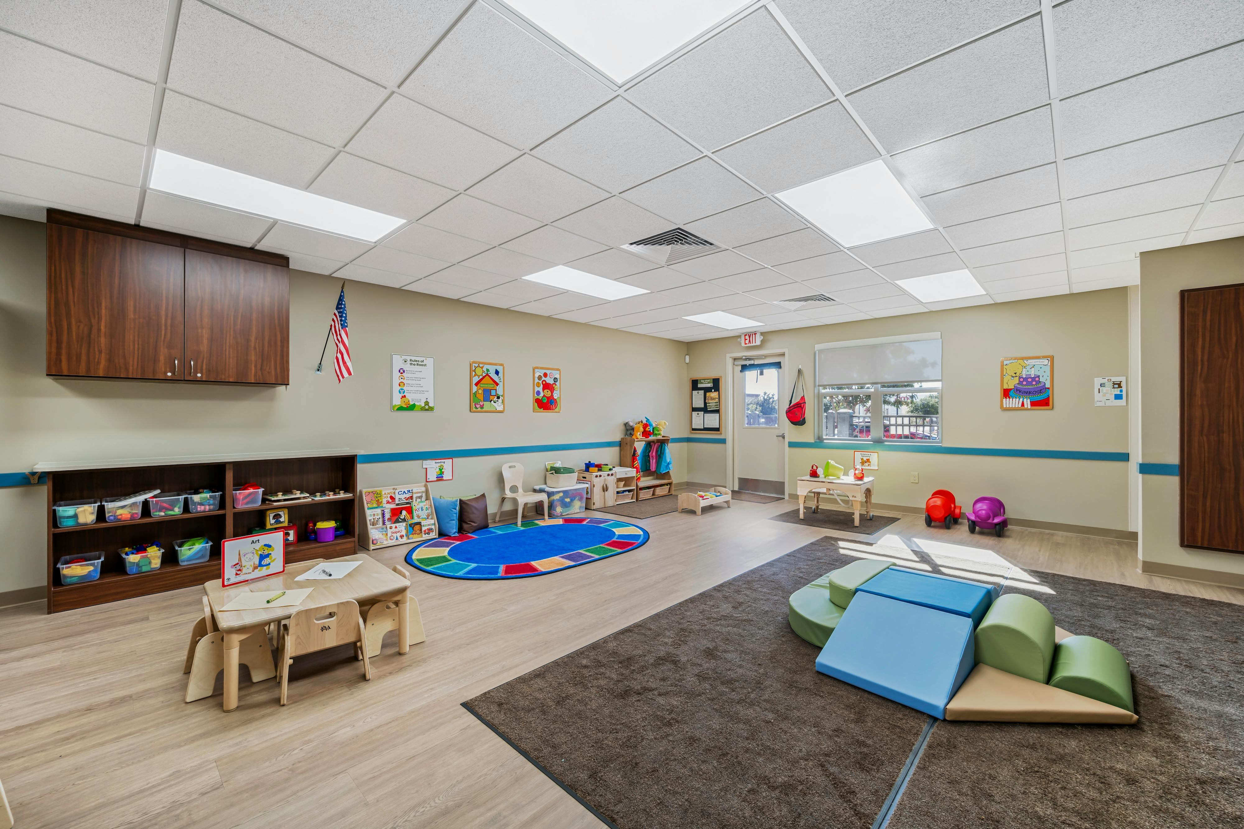 Classroom with small tables, chairs, a colorful rug, and cushioned play structures