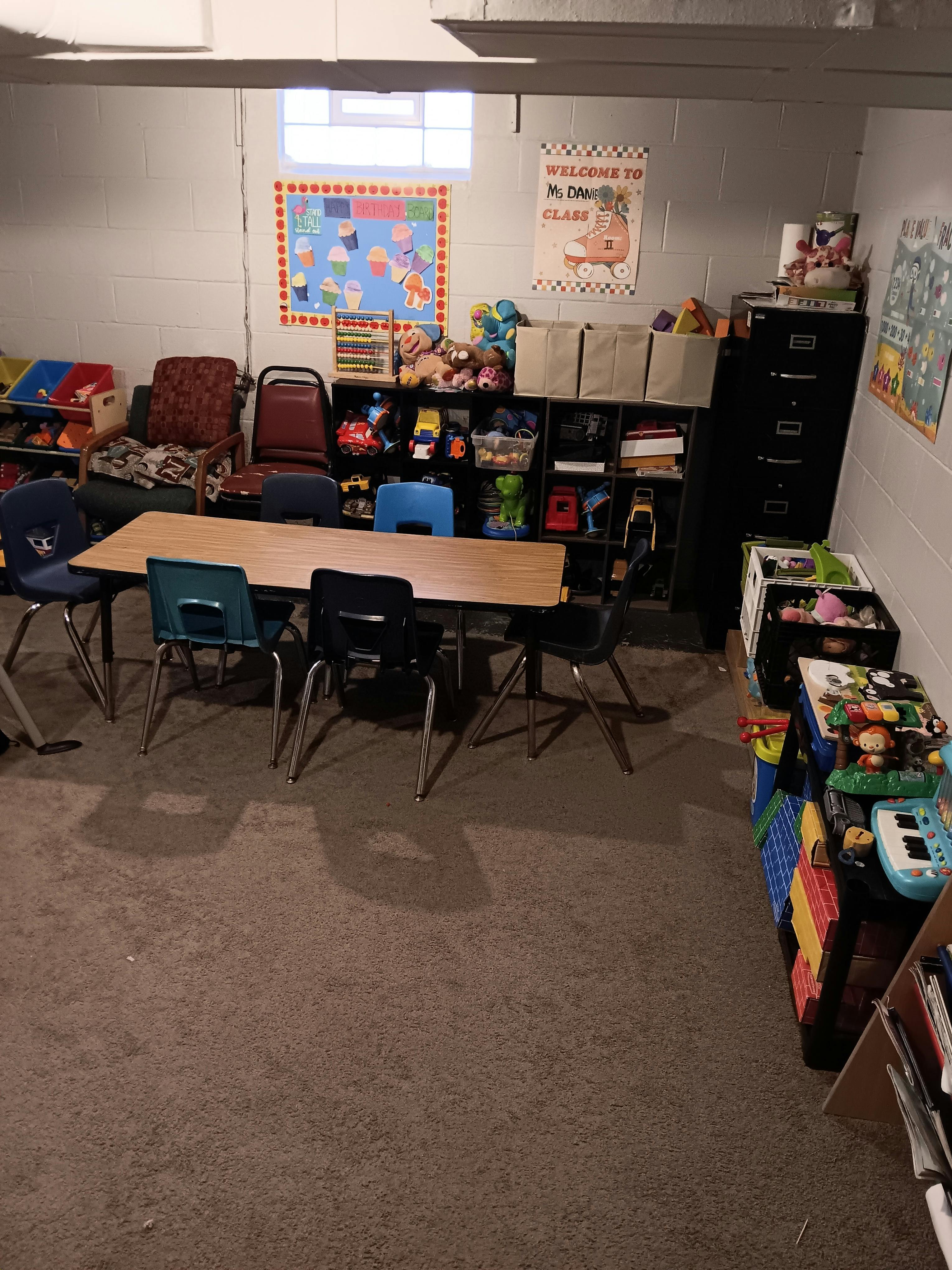 Classroom with a table and chairs, shelves with toys, and posters on the wall