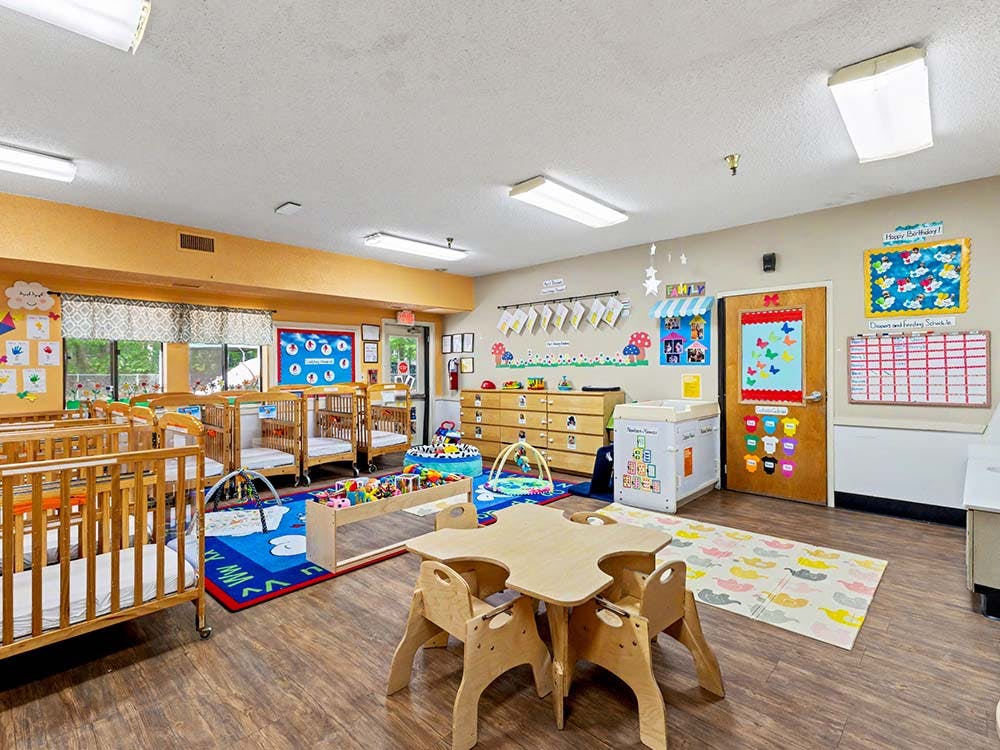 A childcare room with cribs, play mats, and a small table with chairs