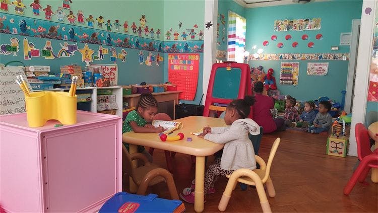 Children in a classroom, some at a table, others on the floor
