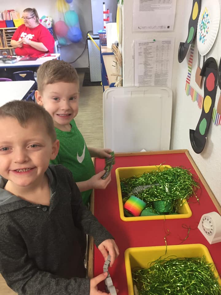 Two children standing at a table with bins of green tinsel