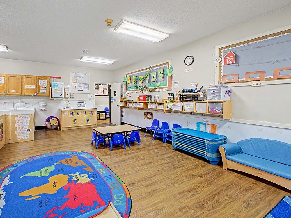 Empty colorful preschool classroom with sinks, tables, chairs, and a world map rug